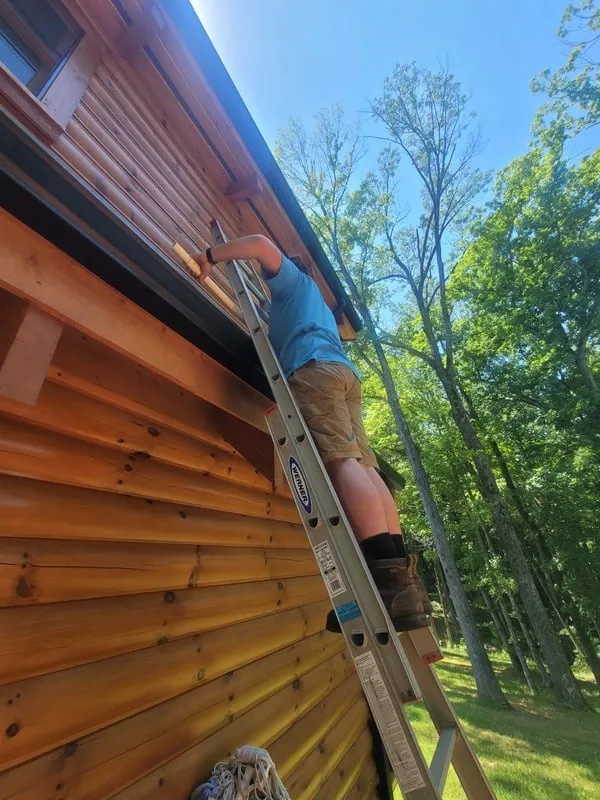 Bush Lackey crew member working from a ladder to clean a cabin gutter